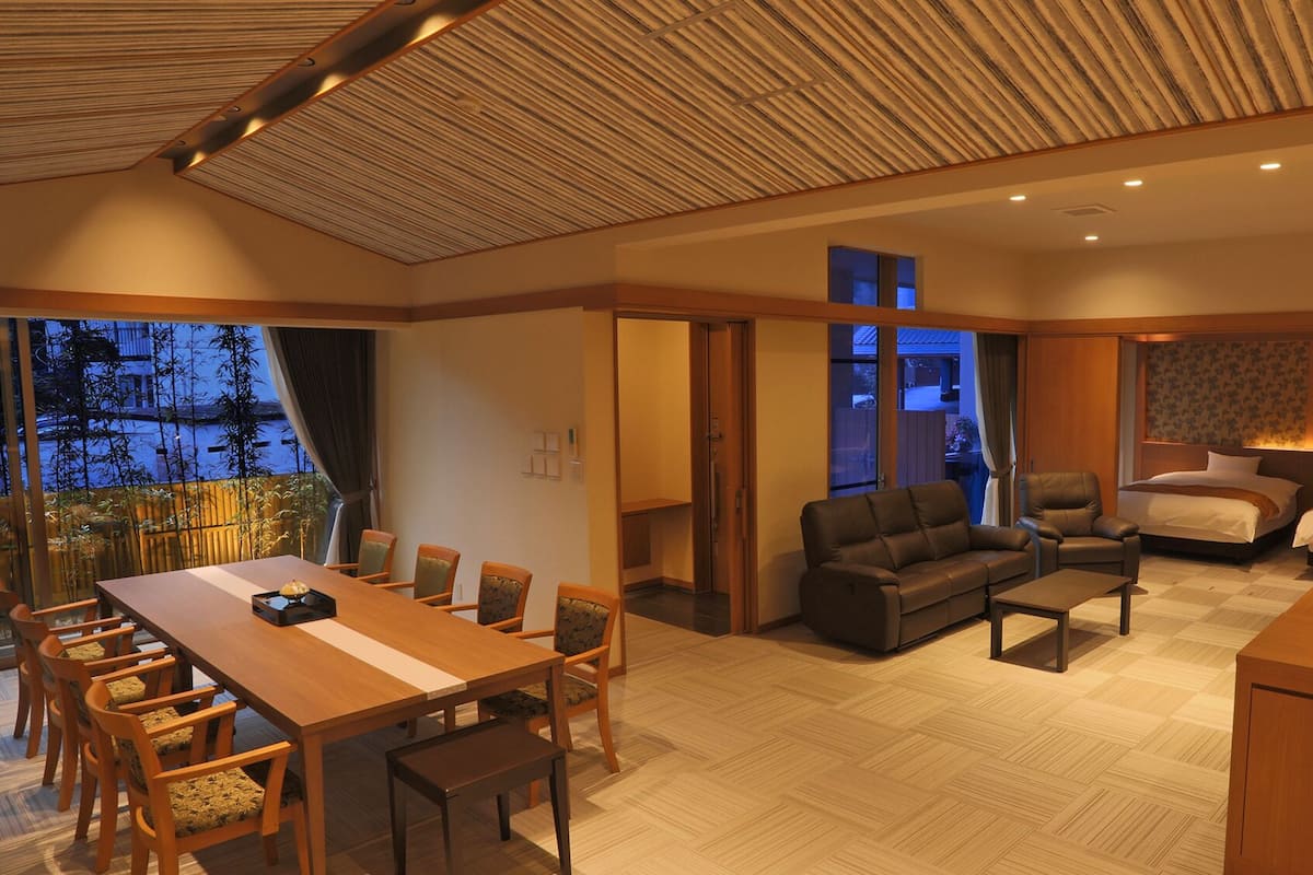 A modern hotel room with a dining area, sofa, and two beds.