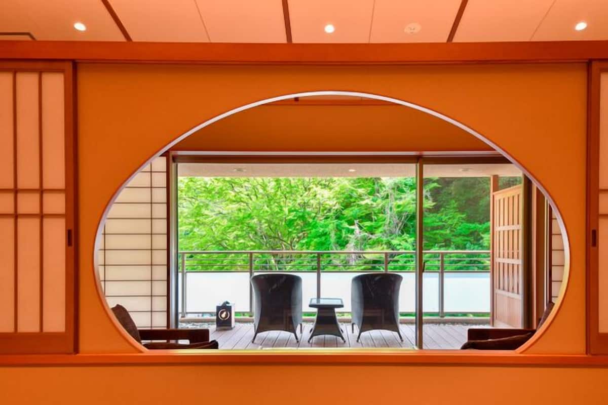 A room with a large oval window, two chairs, a small table, and a view of greenery outside.