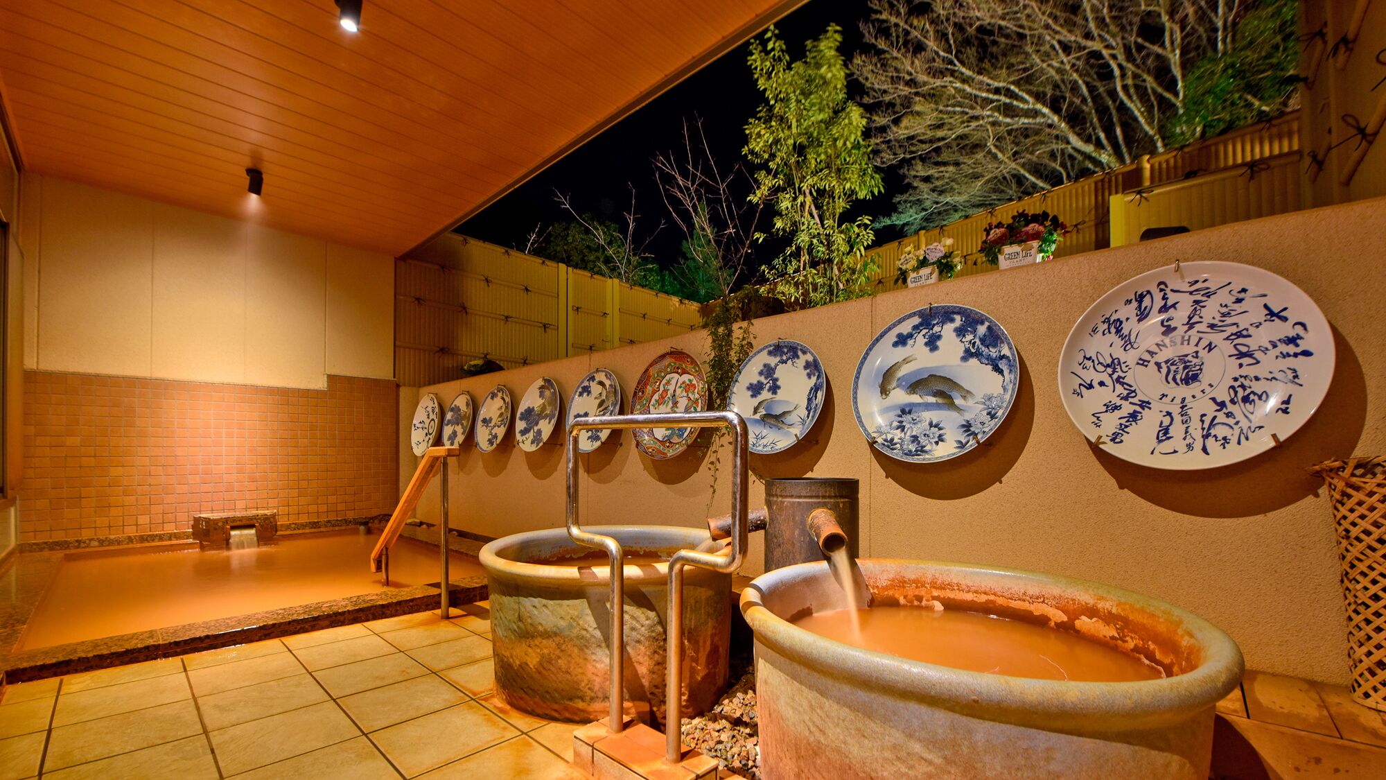A traditional Japanese onsen with stone tubs, a wooden bench, and decorative plates on the wall.