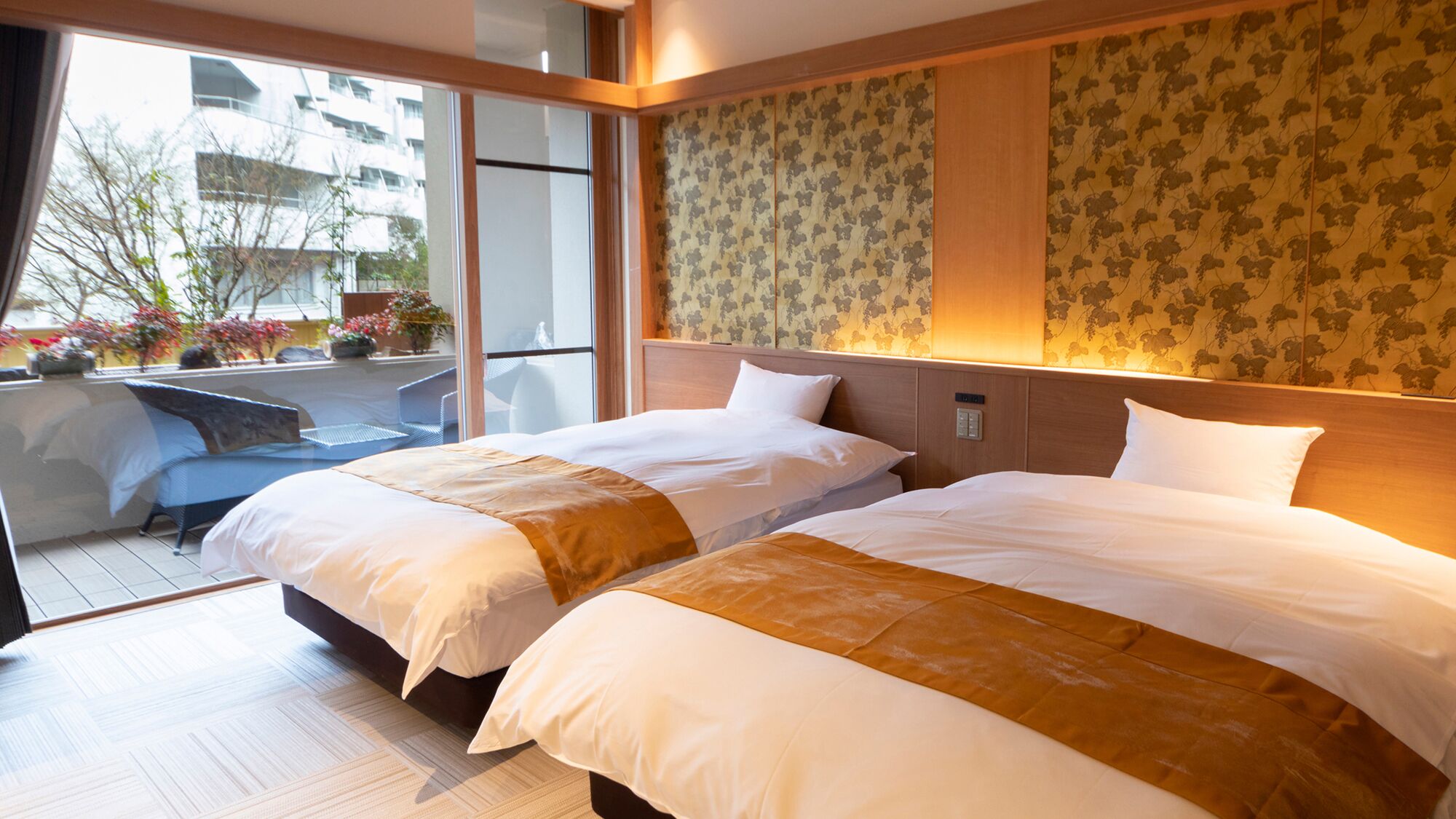 A hotel room with two beds, a balcony with outdoor seating, and a view of the cityscape.