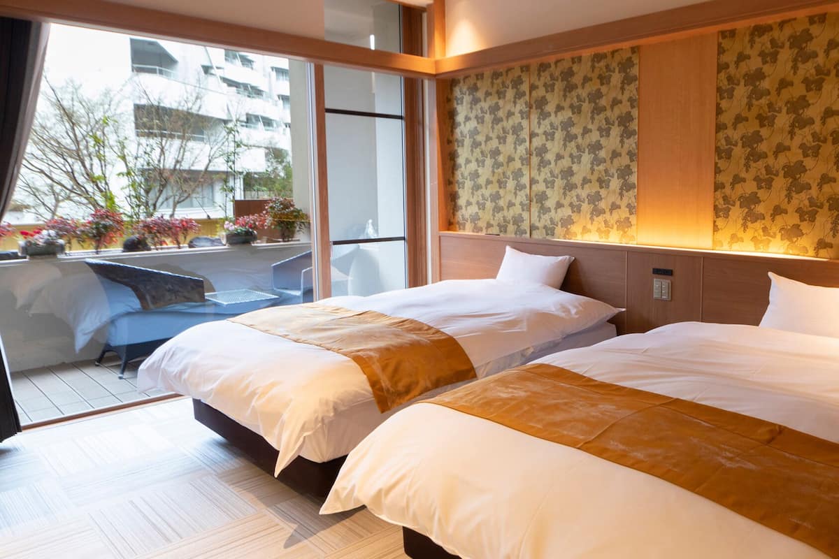 A hotel room with two beds, a balcony with outdoor seating, and a view of the cityscape.