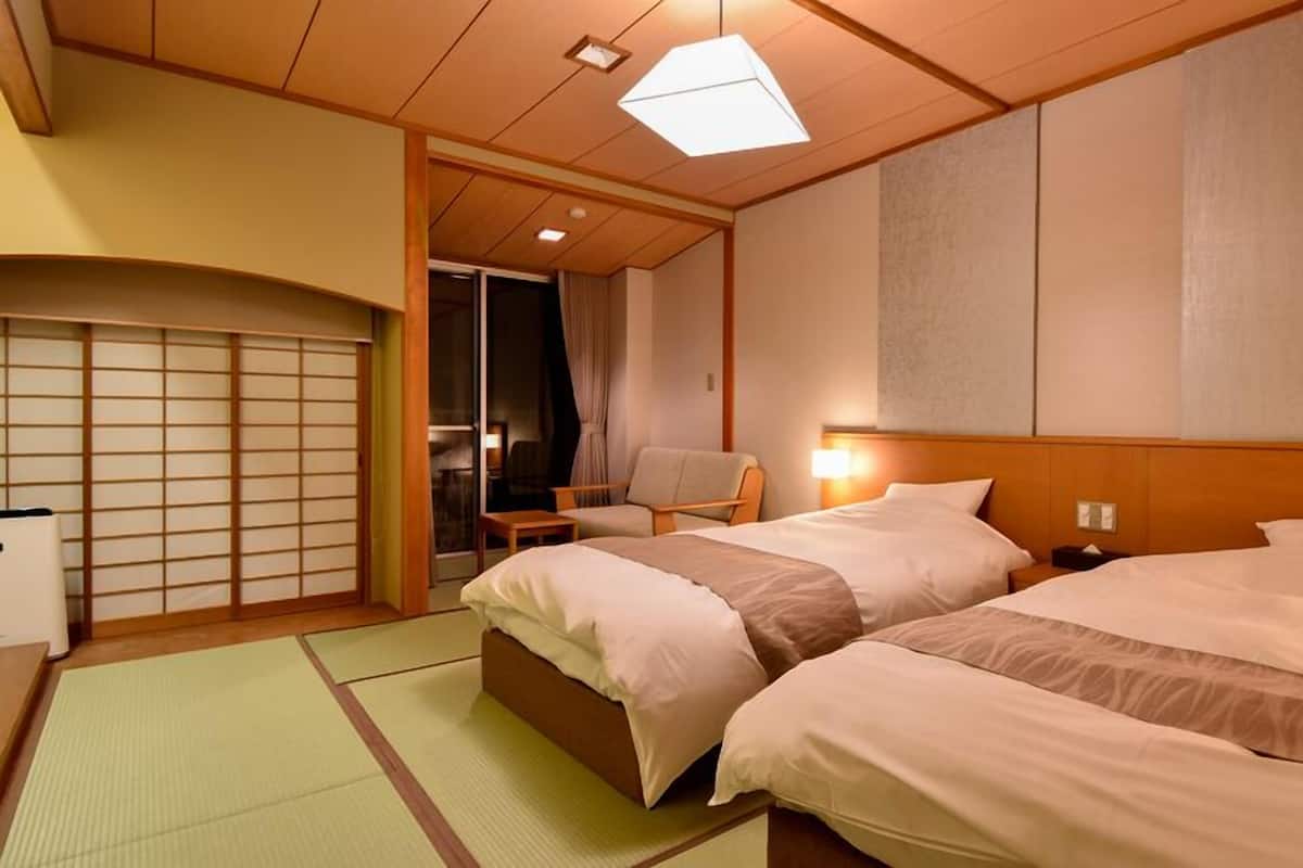 A hotel room with two beds, a traditional sliding door, a chair, and a small table.