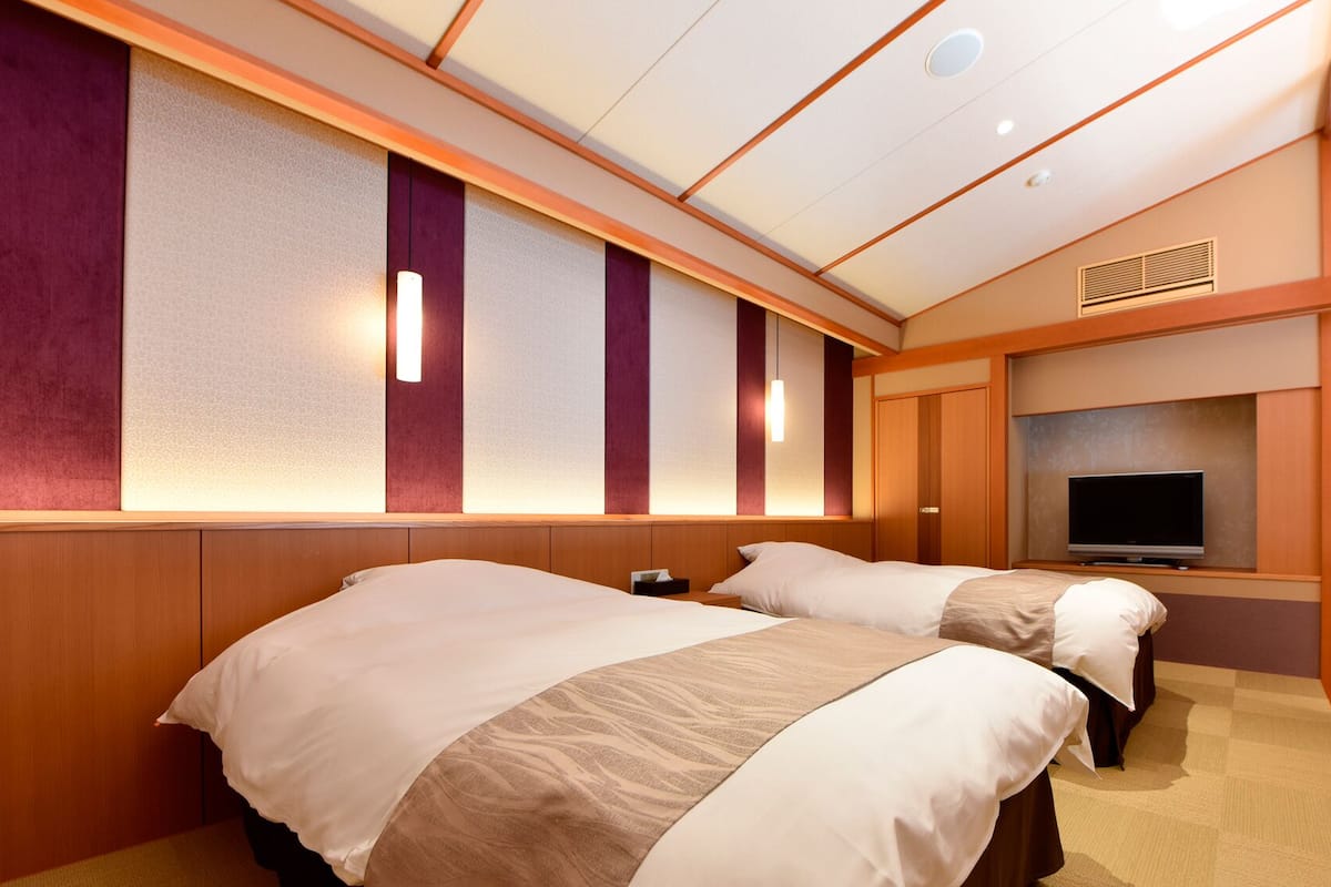 A hotel room with two beds, a television, and a large window.