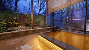 Un espace moderne aménagé à l’extérieur avec un bain à remous, un mur en pierre, une terrasse en bois et des plantes en bambou.