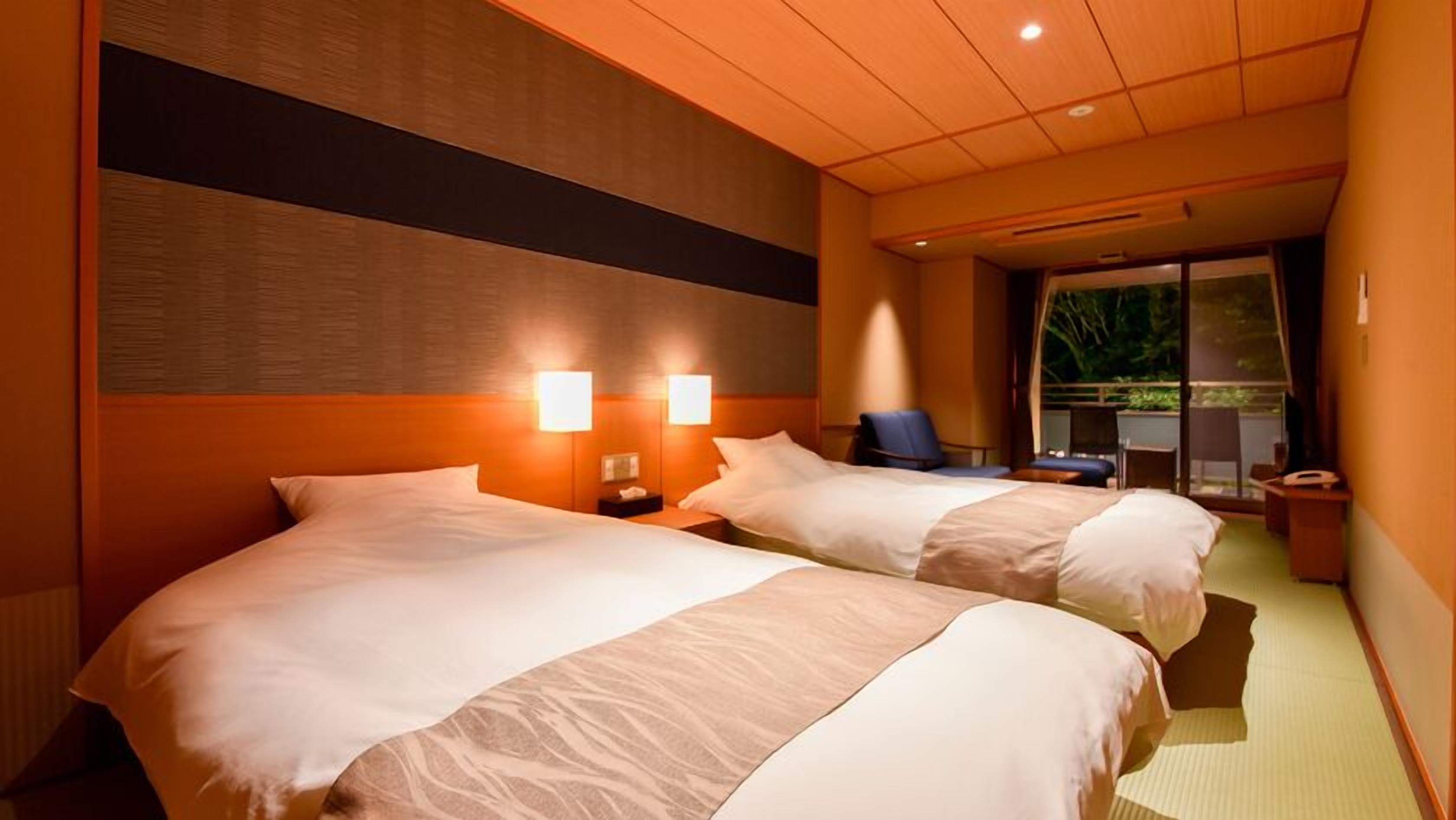 A hotel room with two beds, a desk, a chair, and a view of the outdoors.