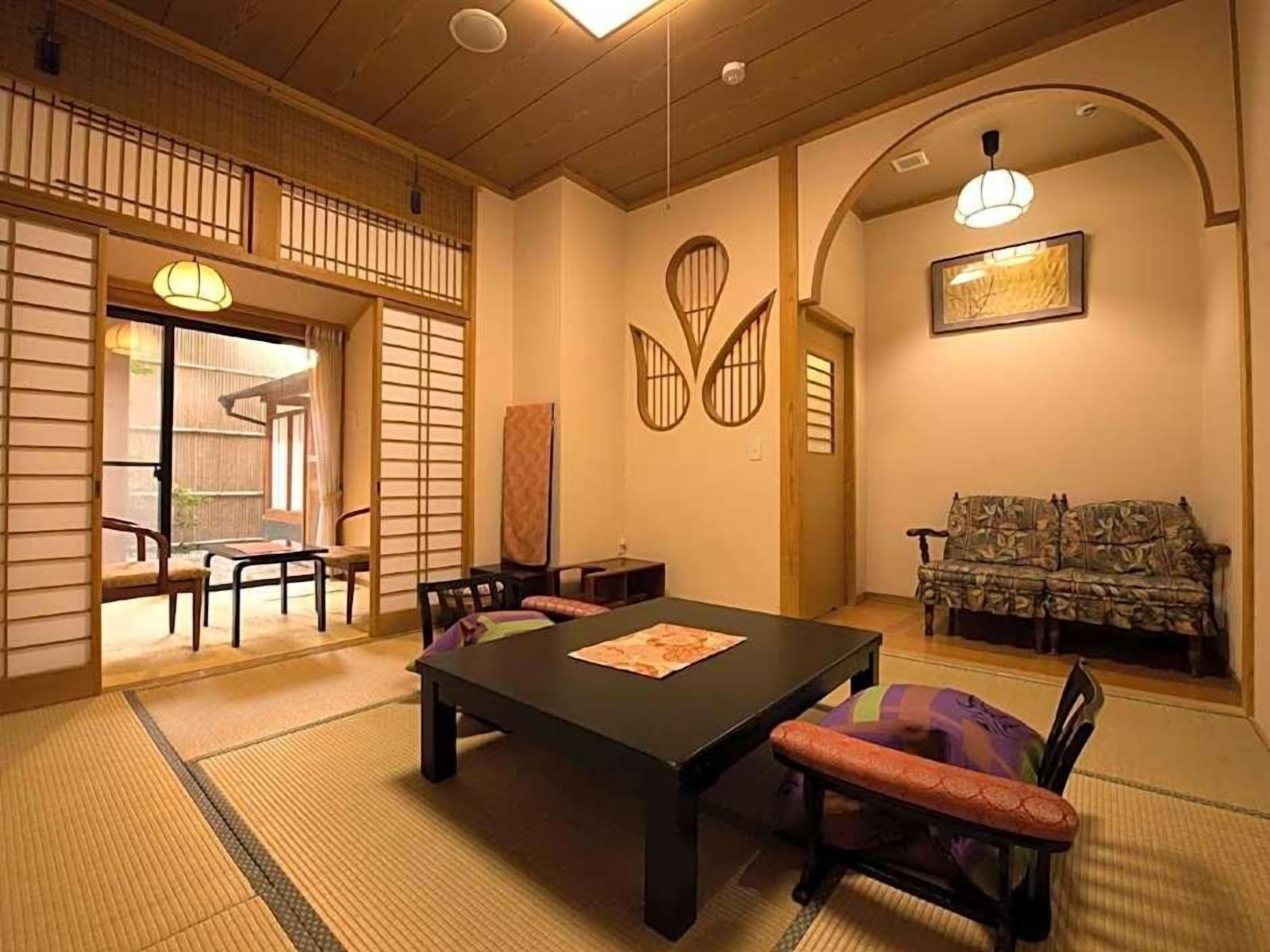 Una habitación tradicional japonesa con suelo de tatami, una mesa baja con cojines y un sofá.
