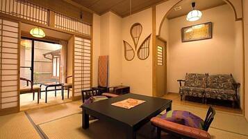 Una habitación tradicional japonesa con suelo de tatami, una mesa baja con cojines y un sofá.