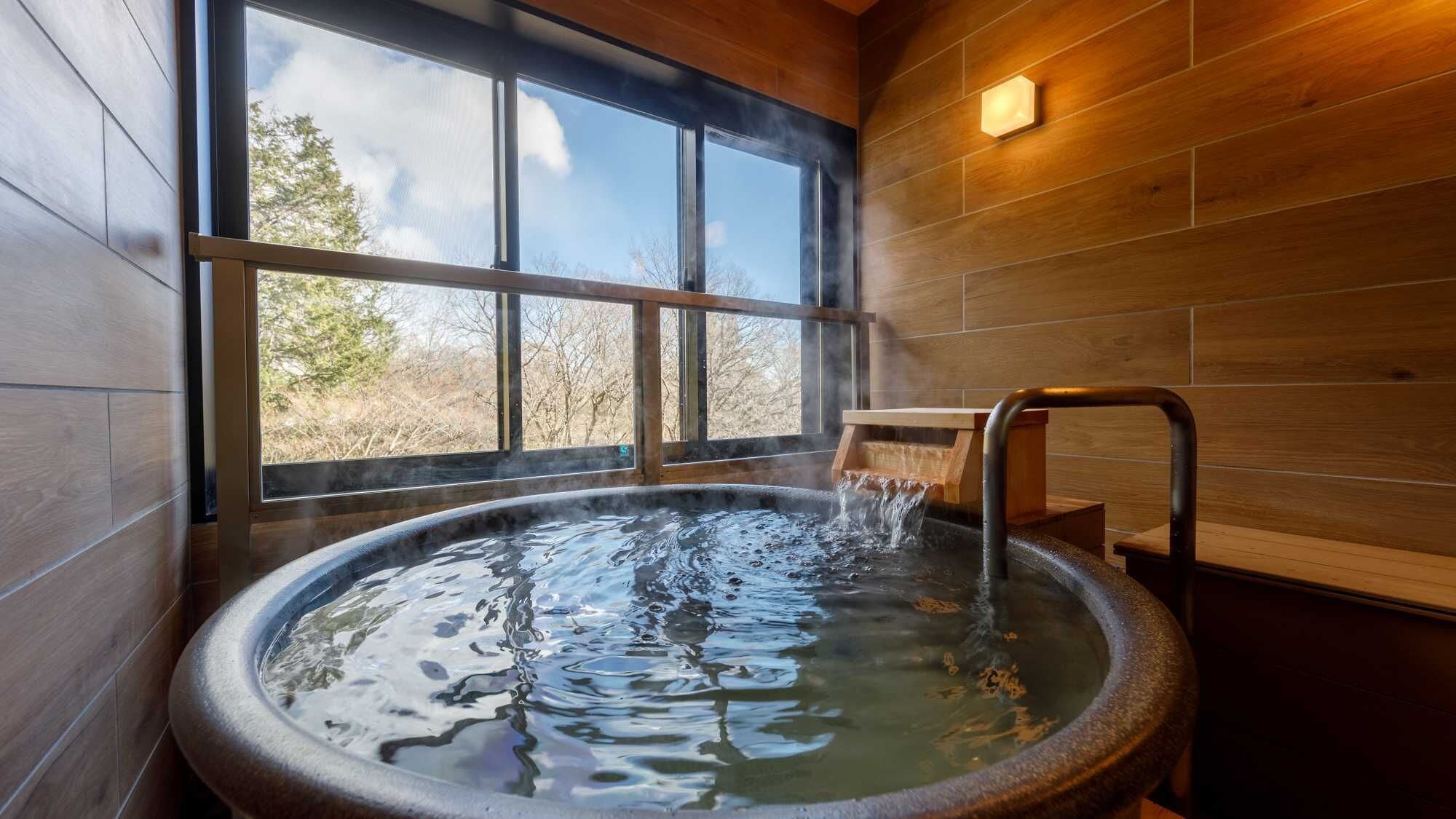 A hot tub with a wooden interior, a window with a view of trees, and a wooden bench.