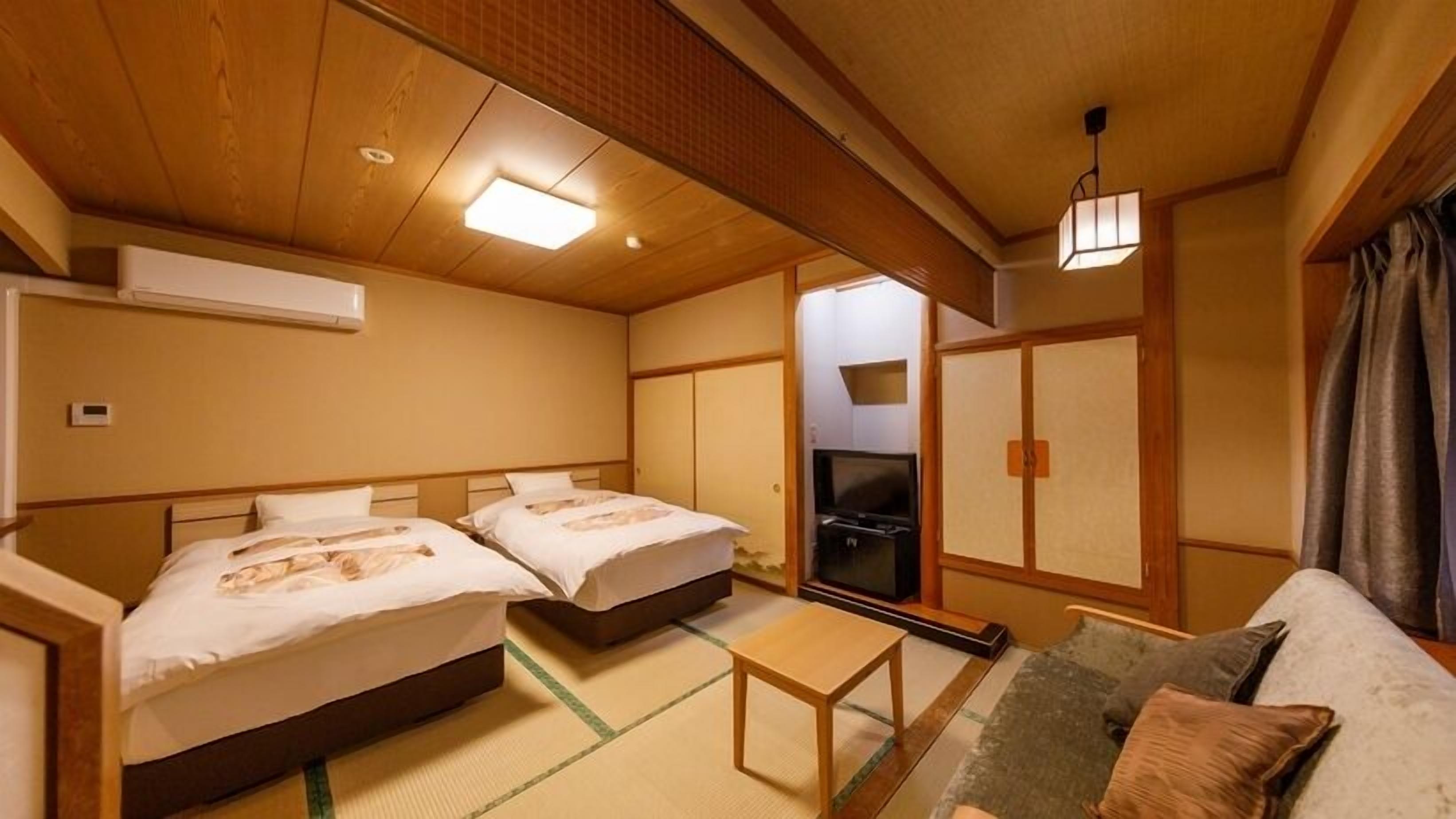 A traditional Japanese-style room with two beds, a TV, tatami flooring, and a futon.