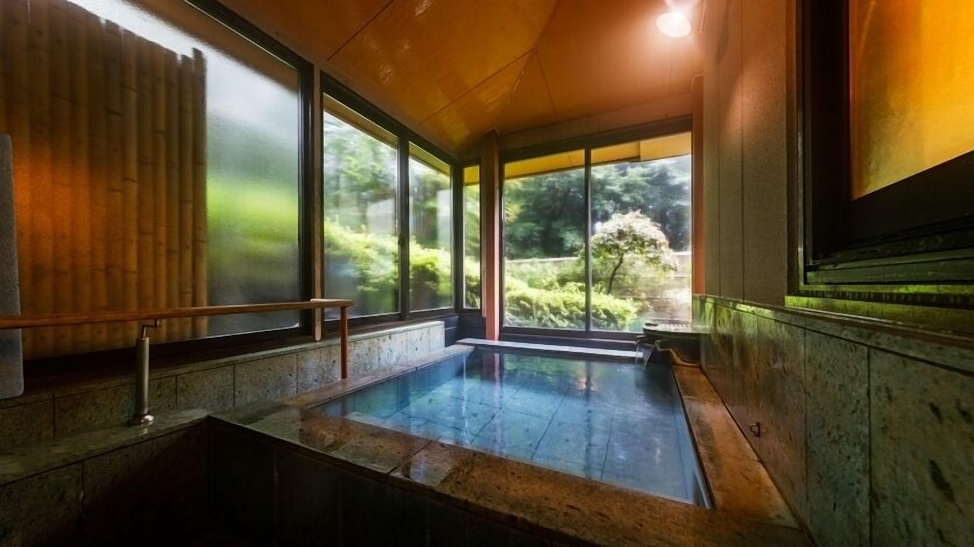 A hot spring bath with a wooden interior, large windows, and a view of greenery outside.