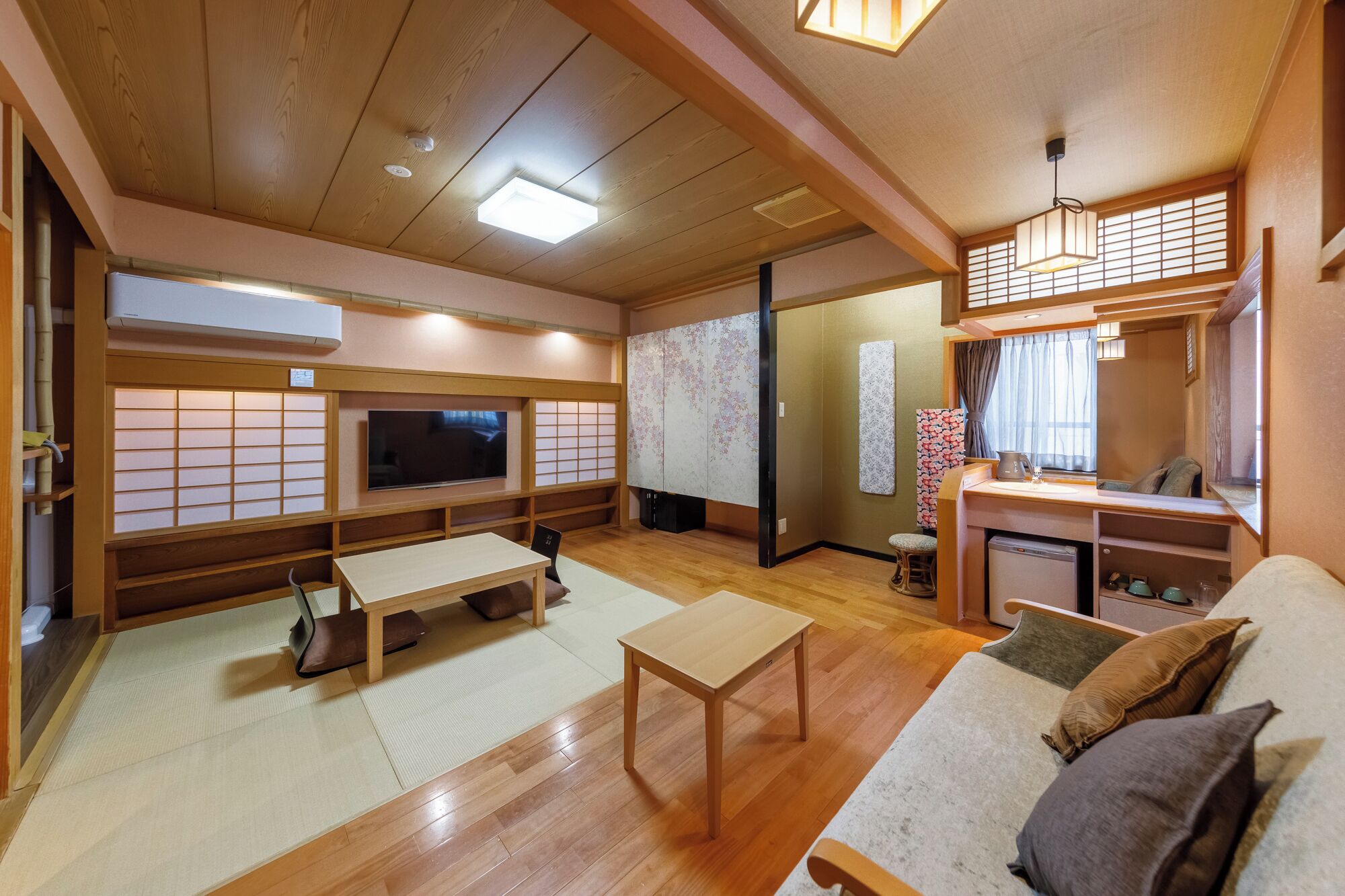 A traditional Japanese-style room with tatami flooring, a low table, a sofa, a television, and a sliding door.