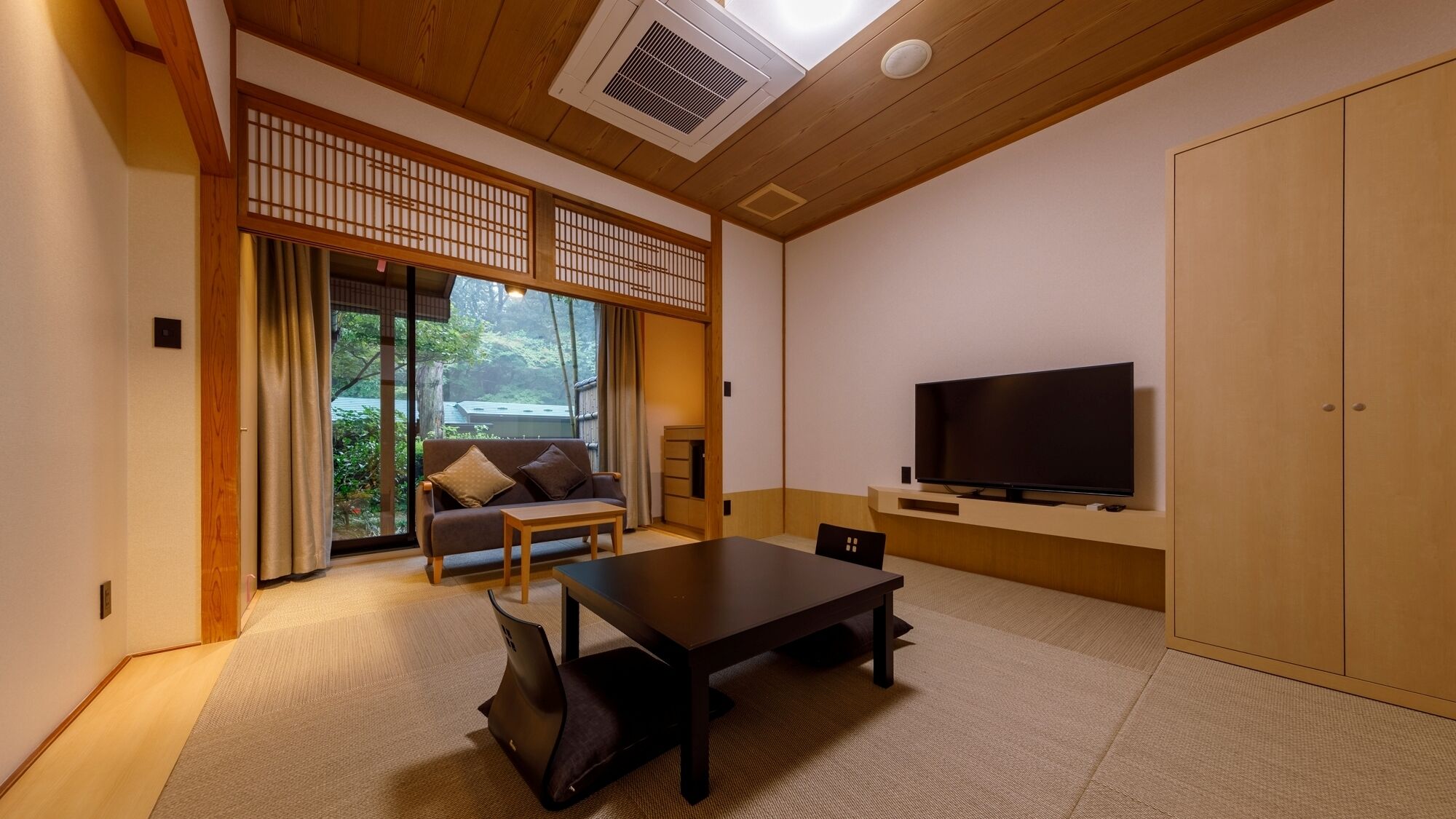 A traditional Japanese-style room with tatami flooring, a sliding door leading to a garden, a sofa, a TV on a wooden stand, and a wardrobe.