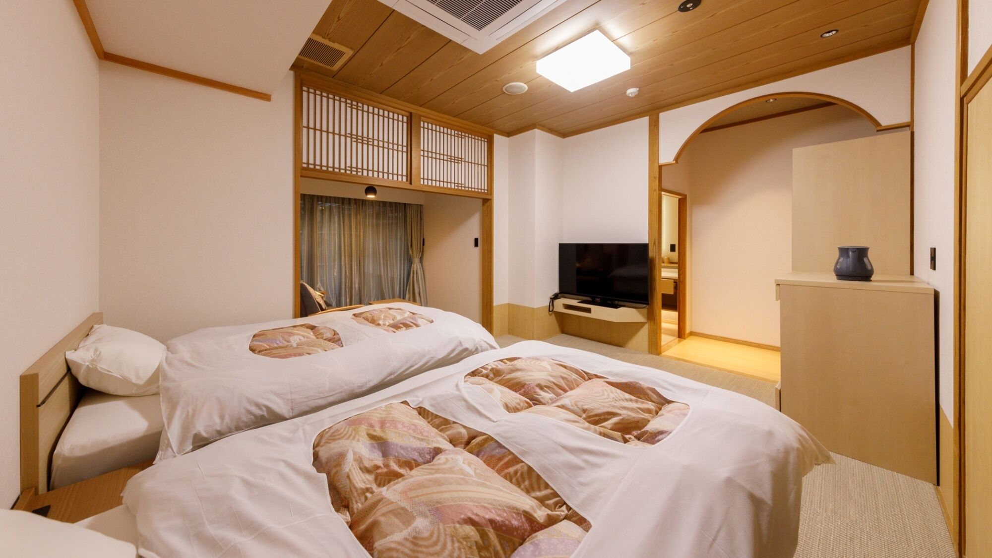 A hotel room with two beds, a TV, a desk, and a mirror.