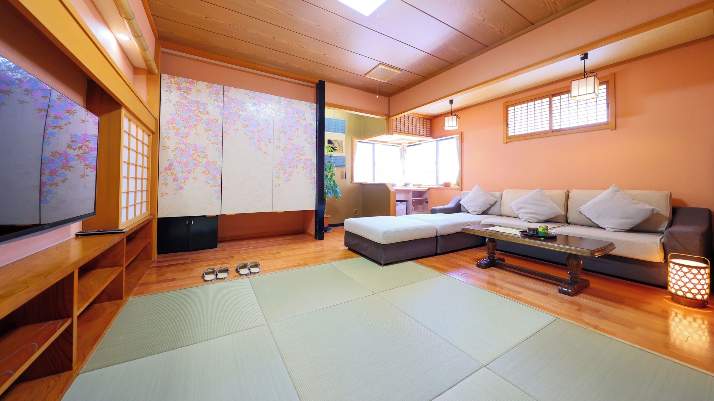 Un salón de estilo japonés tradicional con suelo de tatami, una mesa baja, un sofá y un televisor.