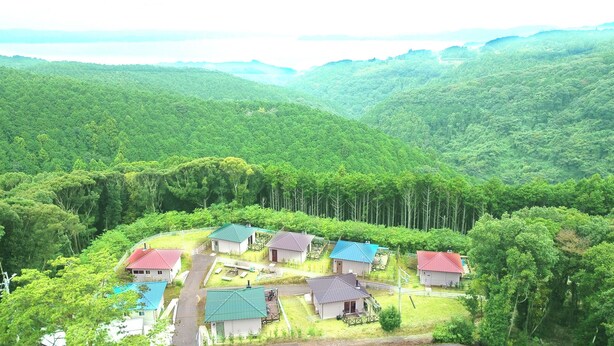Un groupe de maisons aux toits rouges, nichées dans une vallée entourée d’une forêt dense.
