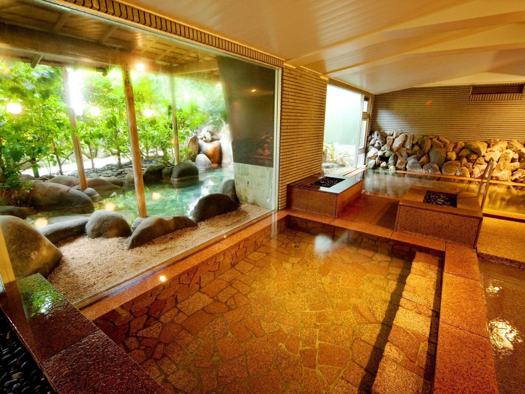 Un interior moderno con un recinto de vidrio que muestra un jardín de rocas naturales y un elemento acuático, suelo de baldosas de piedra y una zona de estar con calefacción integrada.