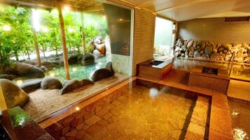 Un interior moderno con un recinto de vidrio que muestra un jardín de rocas naturales y un elemento acuático, suelo de baldosas de piedra y una zona de estar con calefacción integrada.