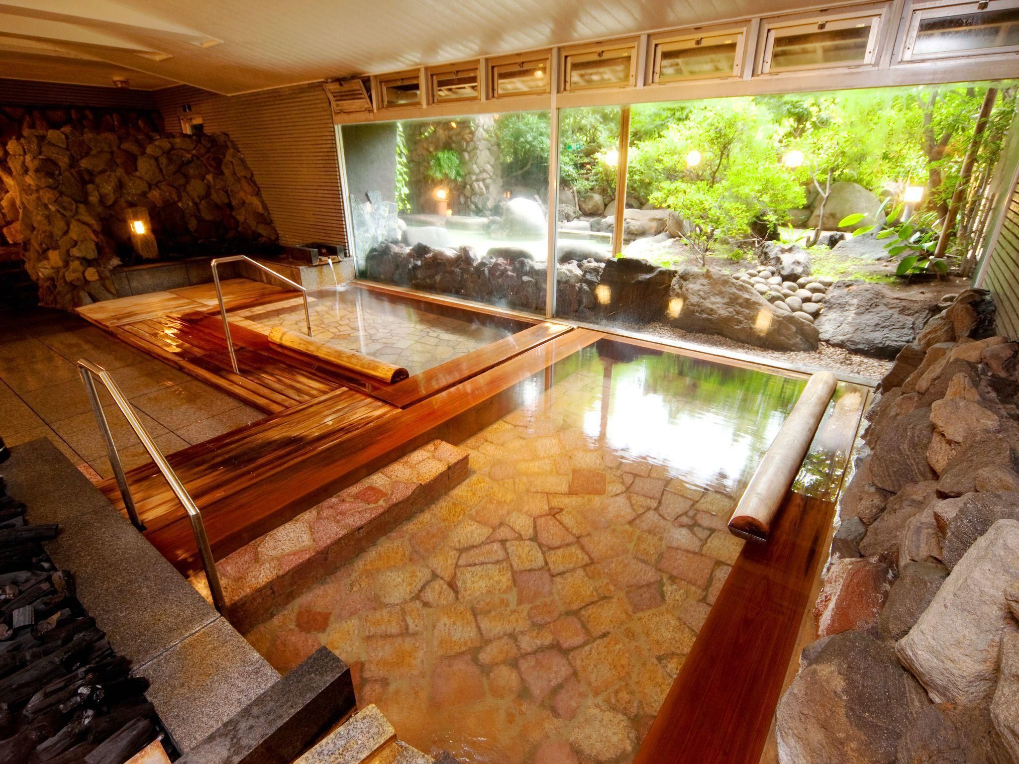 Un onsen japonés tradicional con suelo de piedra, bancos de madera y vistas a un paisaje natural a través de amplios ventanales.