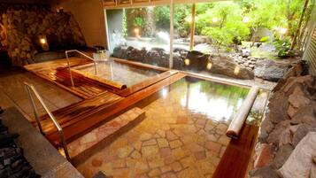 Un onsen japonés tradicional con suelo de piedra, bancos de madera y vistas a un paisaje natural a través de amplios ventanales.
