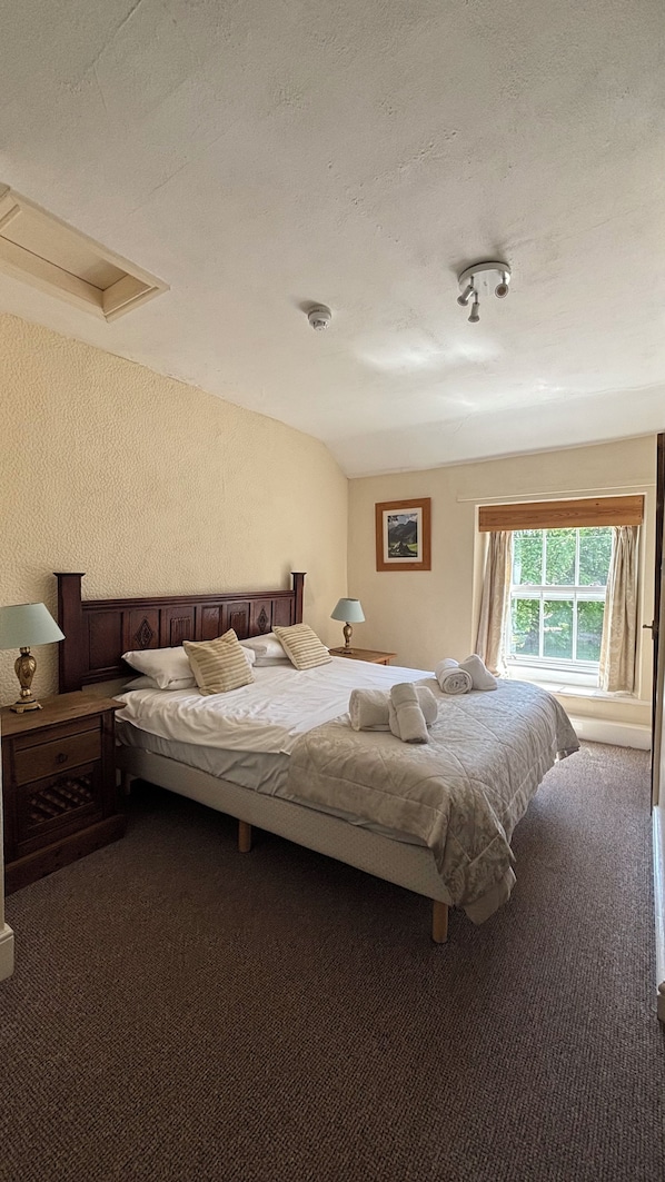 Une chambre à coucher avec un grand lit, deux tables de chevet, une commode, une fenêtre avec des rideaux et un luminaire au plafond.