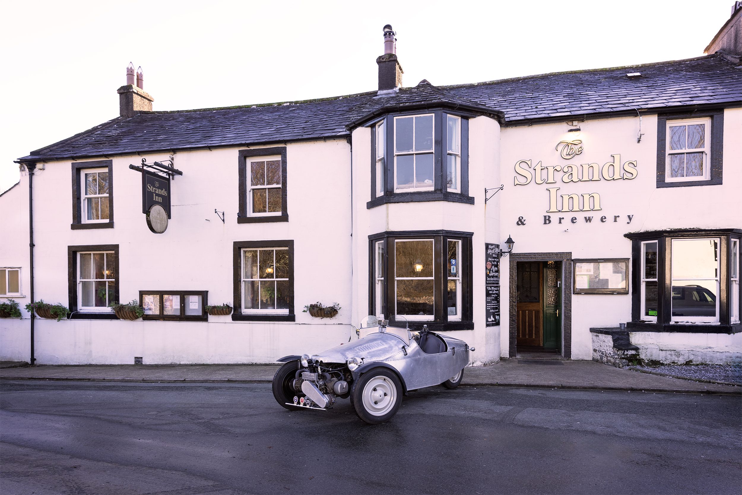 A building with a sign reading 'Strands Inn & Brewery' and a classic car parked in front.