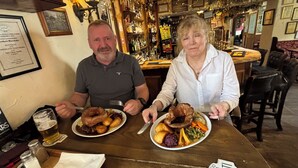 Two people seated at a wooden table with plates of food, a bar in the background, and a framed certificate on the wall. - The Strands & Screes Inn (Seascale)