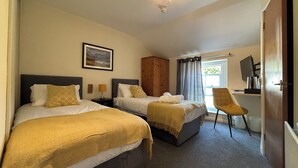 A hotel room with two beds, a wooden wardrobe, a TV, and a chair. - The Strands & Screes Inn (Seascale)