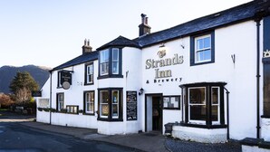 A white building with black trim, a sign reading 'Strands Inn & Brewery,' and a window with a view of the mountains. - The Strands & Screes Inn (Seascale)