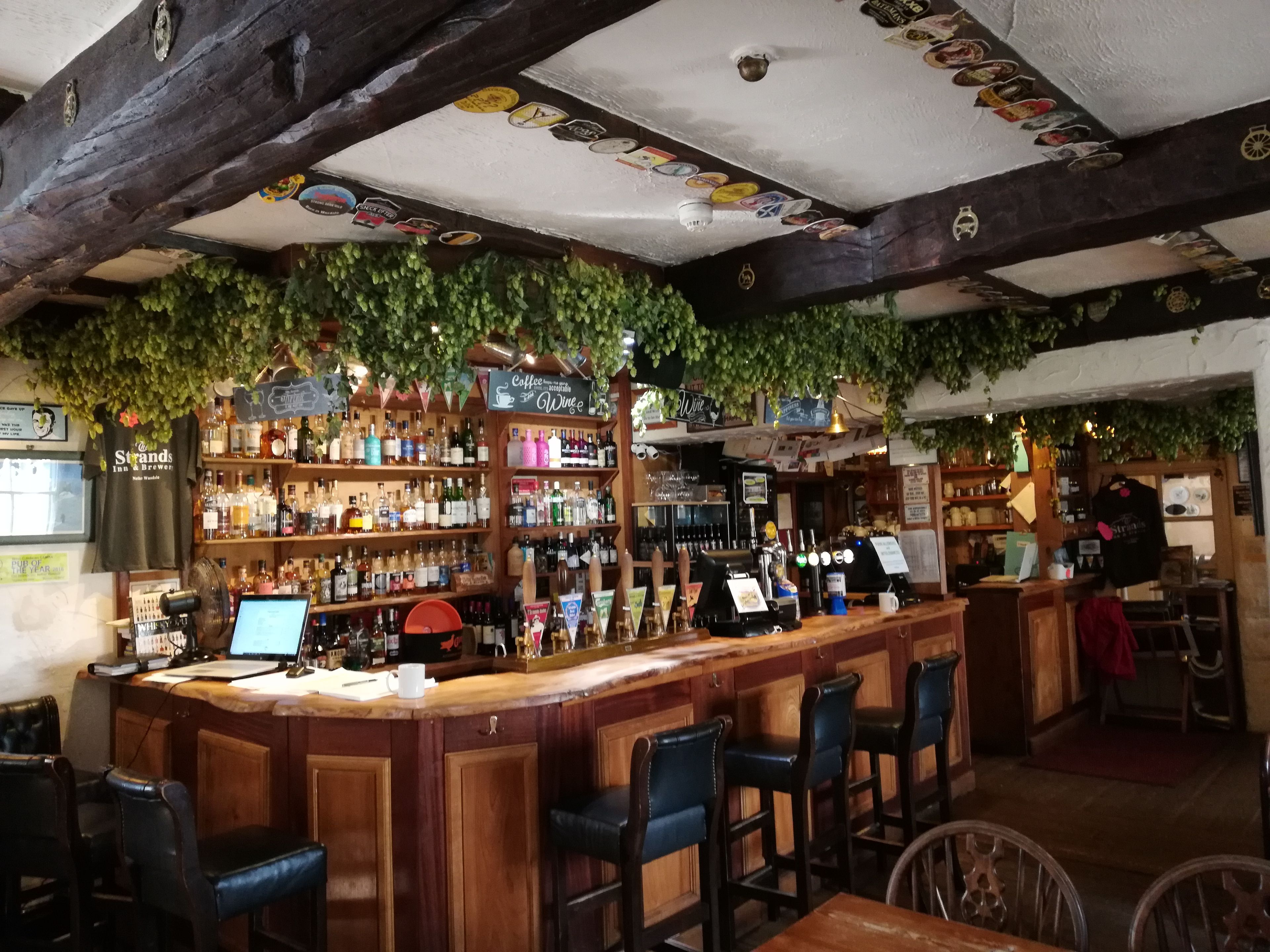 A bar with wooden bar stools, shelves of bottles, and a counter with a computer and a cash register.