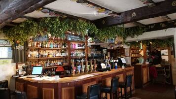 A bar with wooden bar stools, shelves of bottles, and a counter with a computer and a cash register.