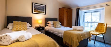 A hotel room with two beds, a wardrobe, a chair, and a window.
