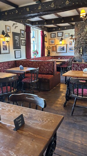 A cozy restaurant interior with wooden tables and benches, stone walls, and various framed pictures. - The Strands & Screes Inn (Seascale)