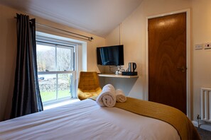 A hotel room with a bed, a chair, a TV, and a view of the outdoors. - The Strands & Screes Inn (Seascale)