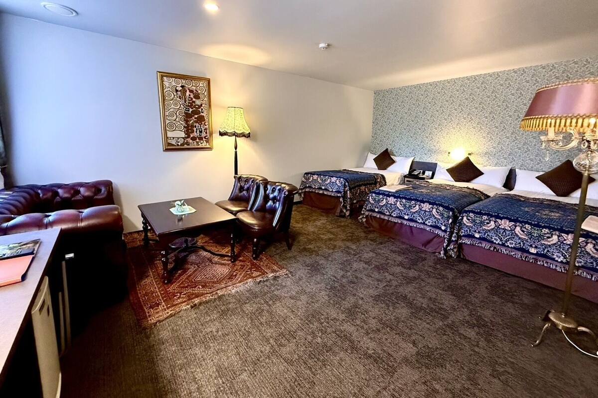 Ein Hotelzimmer mit einer Couch, zwei Einzelbetten, einem Tisch und einer Lampe.