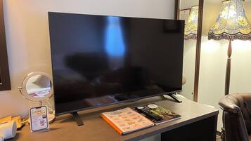 Un televisor de pantalla plana sobre un soporte, una lámpara, un espejo y una revista sobre una mesa.