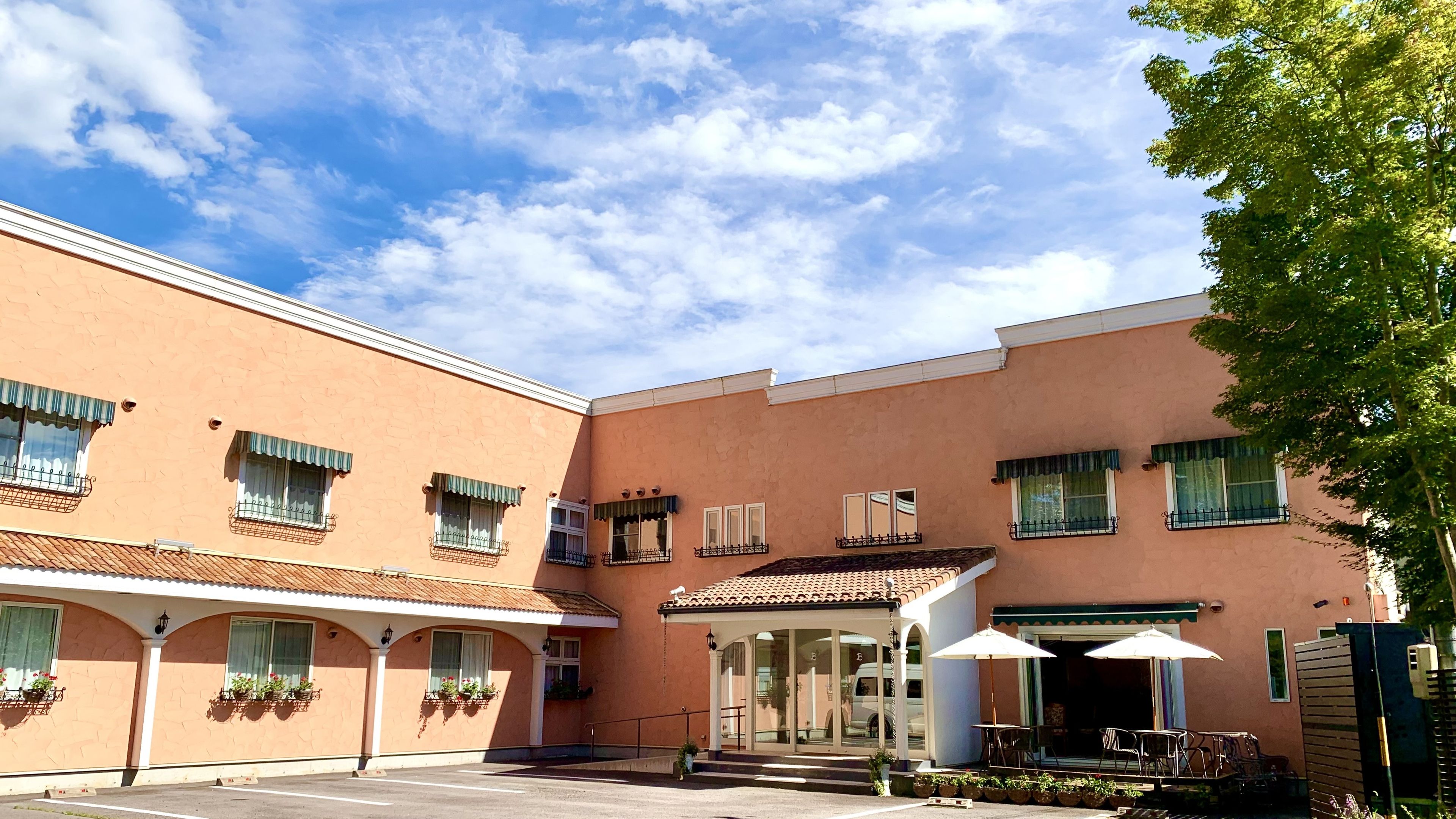 Un edificio con patio, múltiples ventanas con toldos y mobiliario exterior con sombrillas.