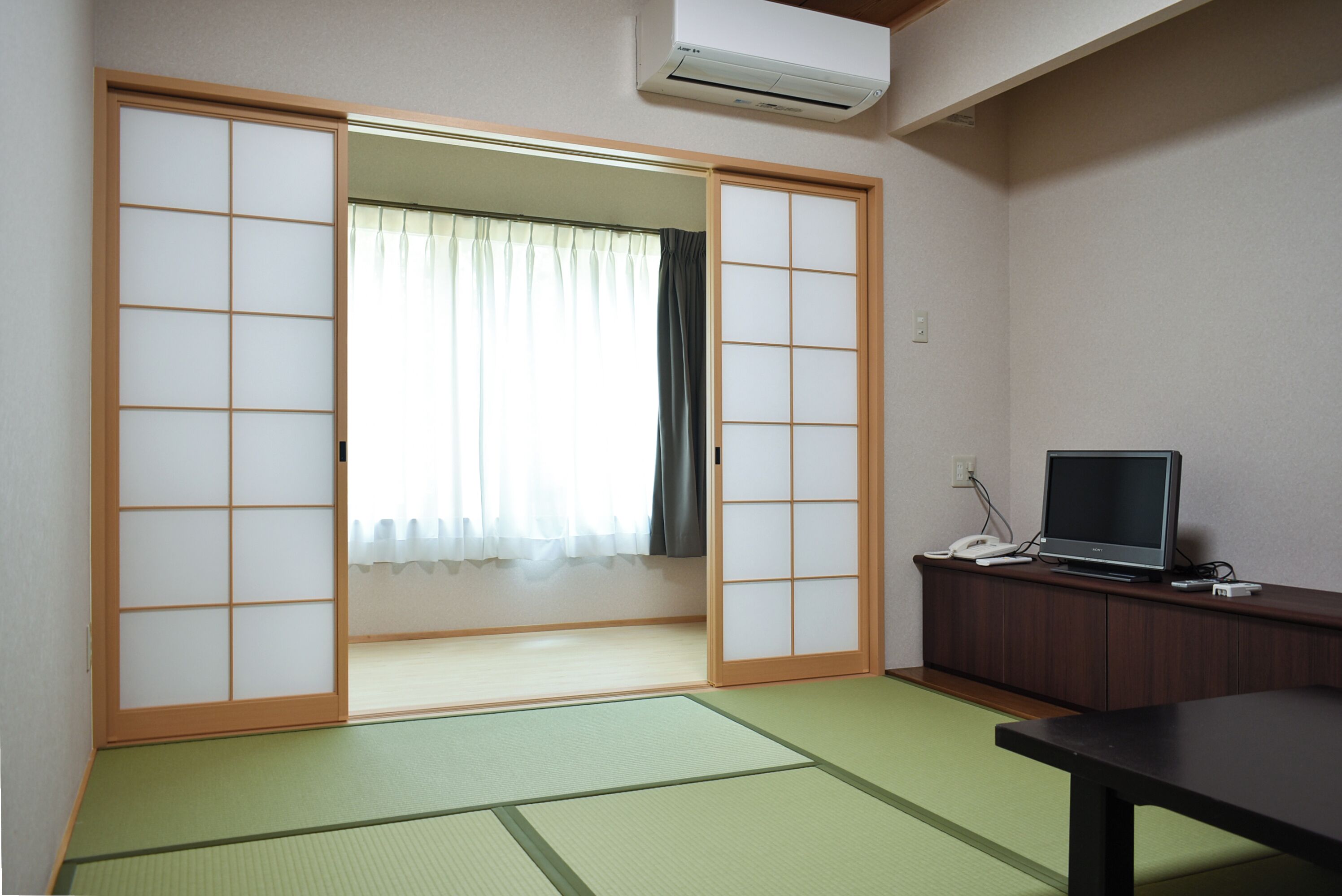 Een kamer met tatami vloer, een schuifdeur van shoji-papier, een televisie op een houten kastje en een kleine tafel.