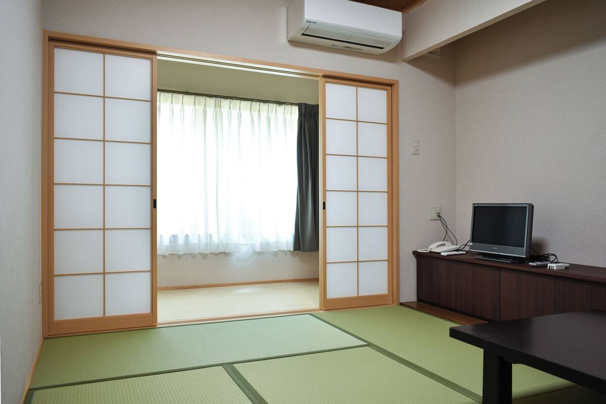 Een kamer met tatami vloer, een schuifdeur van shoji-papier, een televisie op een houten kastje en een kleine tafel.