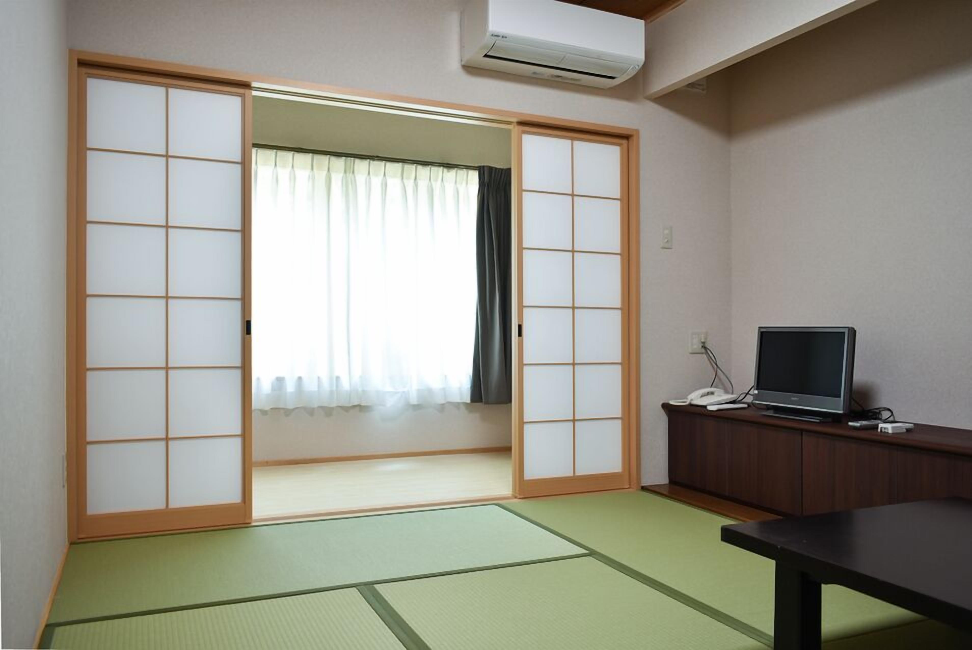 A room with tatami flooring, a sliding door, a television on a wooden cabinet, and a window with curtains.
