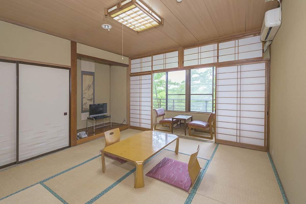 A traditional Japanese room with tatami flooring, a low table, a TV, sliding doors, and a view of greenery.