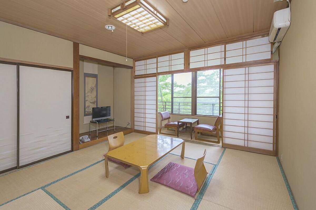 Een traditionele Japanse kamer met tatami vloerbedekking, een lage tafel, een televisie en schuifdeuren.