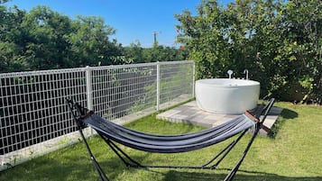 A hammock in a grassy area with a white outdoor hot tub and a metal fence.
