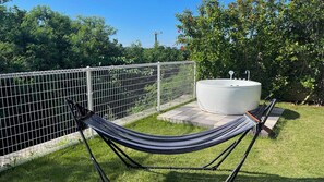 A hammock in a grassy area with a white outdoor hot tub and a metal fence.