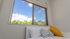 Una habitación con cama, ventana y vista a follaje.