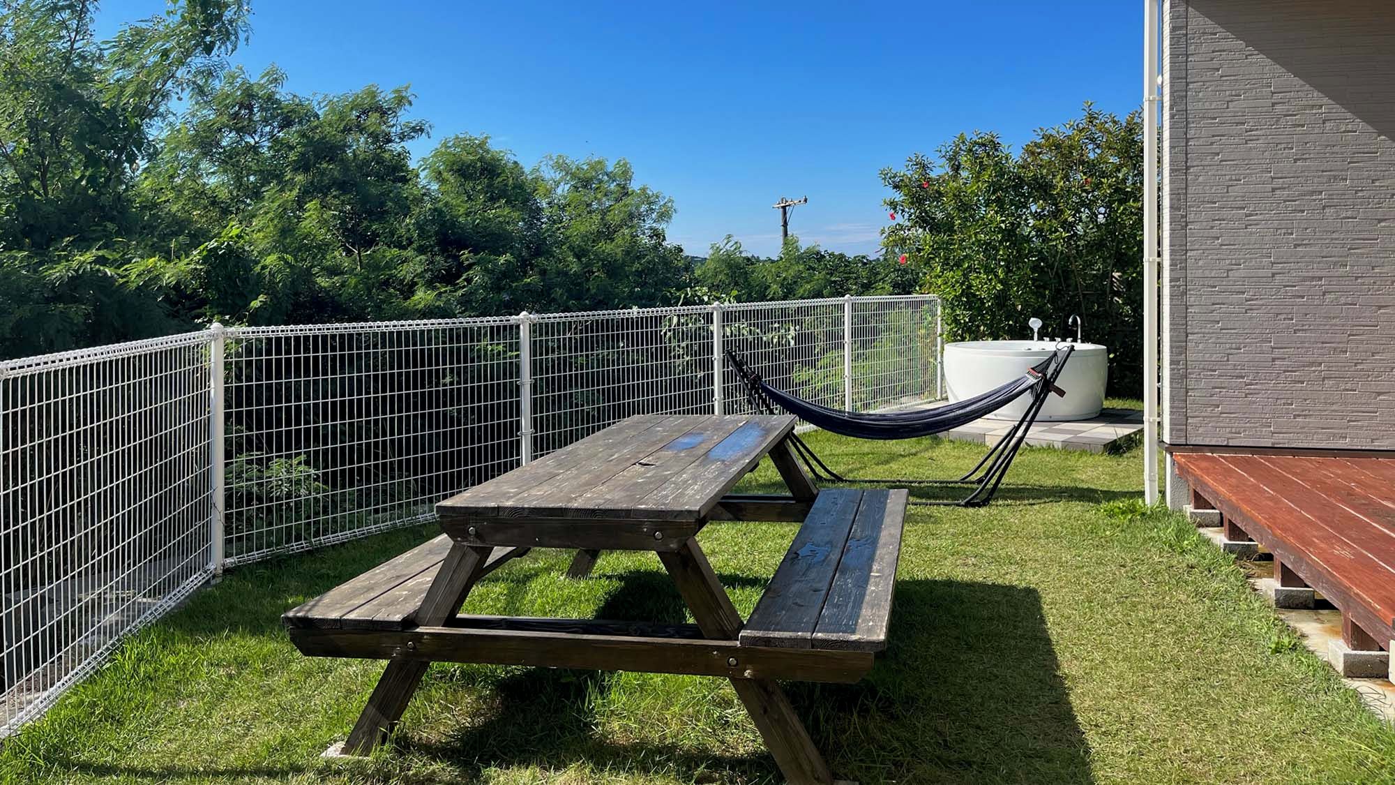 A picnic table with benches and a hammock in a fenced outdoor area.