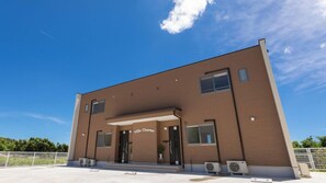 A modern building with a flat roof, a central entrance, and a sign reading 'Villa Charme.' - Villa Charme (Motobu)