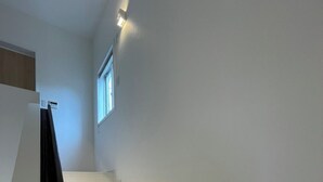 A staircase with white steps leading to a landing, a small window, and a wall-mounted light fixture. - Sunset Resort Kanutan (Motobu)