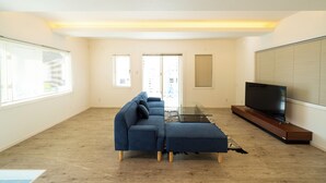 A modern living room with a sectional sofa, a glass coffee table, and a flat-screen TV on a wooden stand. - Sunset Resort Kanutan (Motobu)
