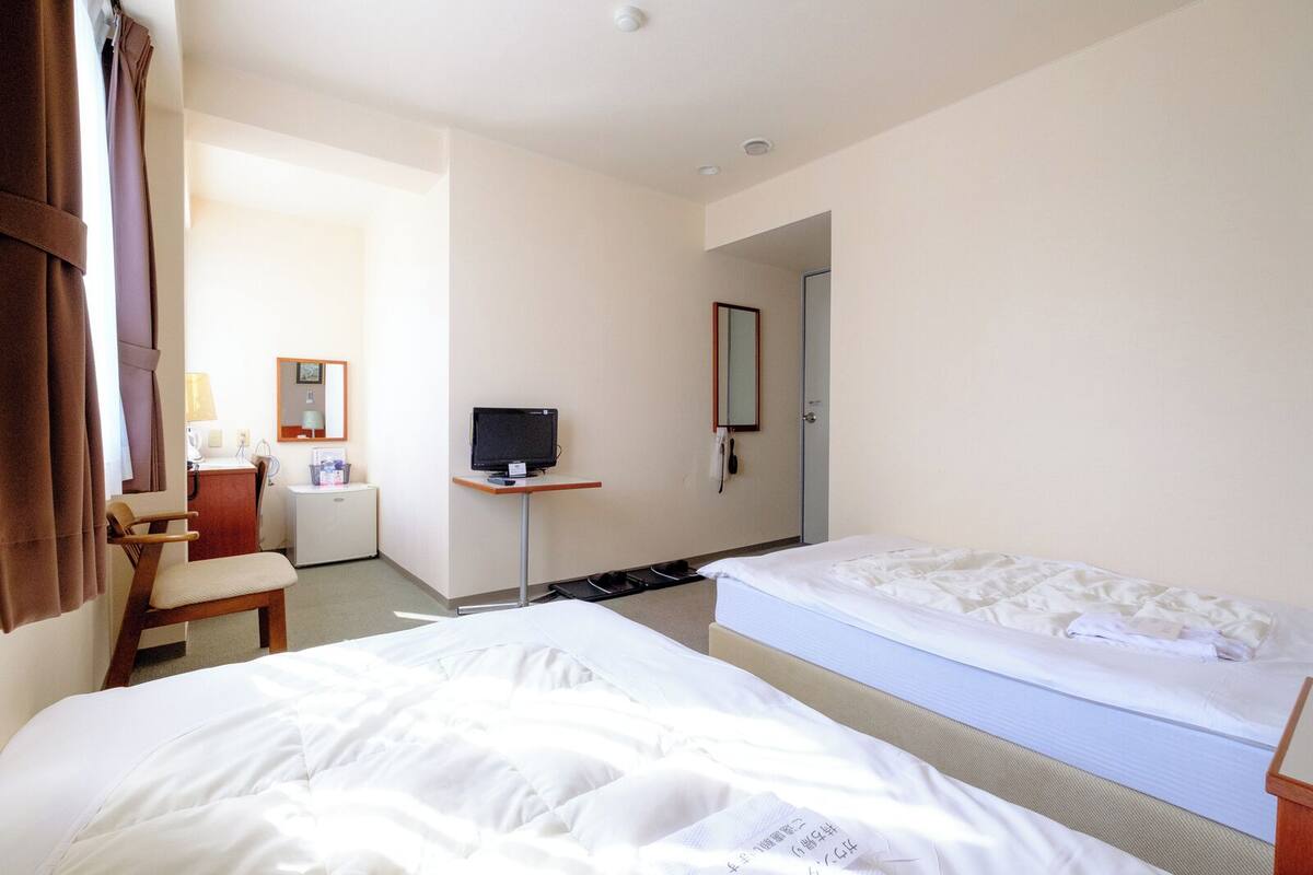 A hotel room with two beds, a desk, a chair, a TV, and a door leading to another room.