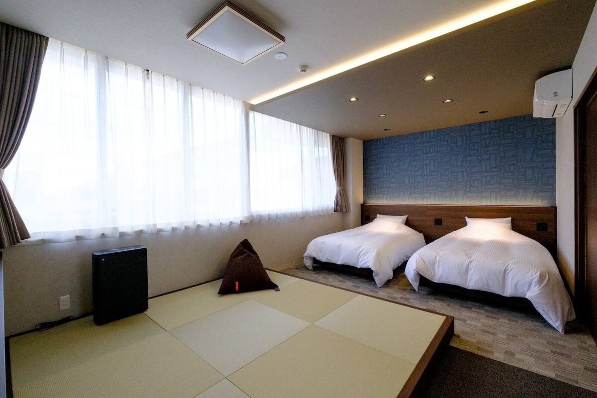 A hotel room with two beds, a tatami mat, a speaker, and a patterned wall.